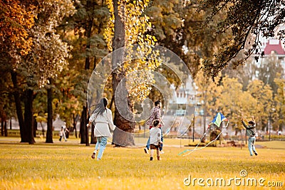 Family with two children flying a kite and running across grassy lawn Stock Photo