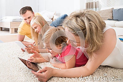 Family using tablets lying on carpet Stock Photo