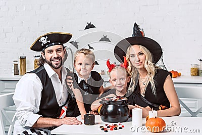 family in various halloween costumes at table with black pot with treats in kitchen Stock Photo