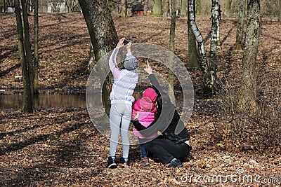 Family for a walk. Dad shows daughter on squirrel, which sits on tree. Girl takes pictures of the squirrel on the phone. Stock Photo