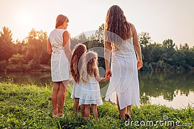 Family walking by summer river at sunset. Mother, grandmother and kids admiring landscape. Women`s day Stock Photo