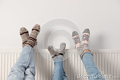 Family warming legs on heating radiator near white wall, closeup Stock Photo