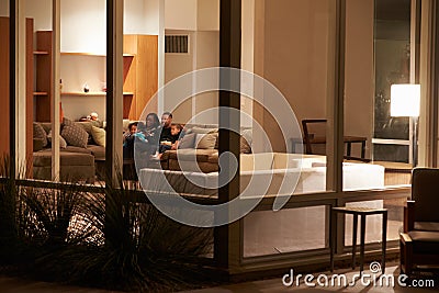 Family Watching TV At Home Viewed From Outside Stock Photo