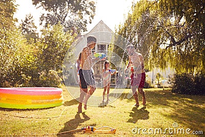 Family Wearing Swimming Costumes Having Water Fight With Water Pistols In Summer Garden Stock Photo