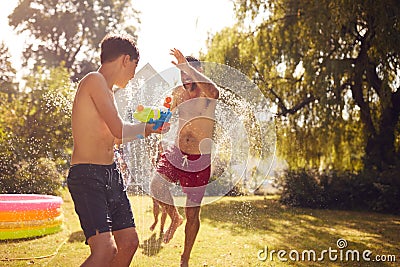 Family Wearing Swimming Costumes Having Water Fight With Water Pistols In Summer Garden Stock Photo