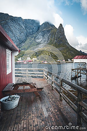 Famous tourist attraction of Reine in Lofoten, Norway with red rorbu houses, clouds, rainy day with bridge and grass and Stock Photo