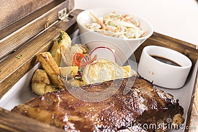 Fancy dish with grilled pork ribs, barbecue sauce, French fries, Coleslaw salad, in a wooden box Stock Photo