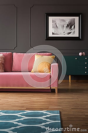 Fancy dresser with golden elements and a velvet pink sofa on hardwood floor in a vintage living room interior with gray walls. Rea Stock Photo