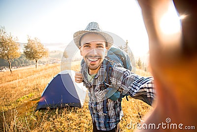 Fanny bearded man with backpack smiling and taking selfie in mountains from his smart phone. Traveler man with beard wearing hat Stock Photo