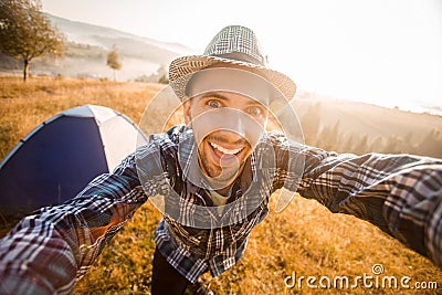 Fanny bearded man smiling and taking selfie in mountains from his smart phone. Traveler man with beard wearing hat take Stock Photo