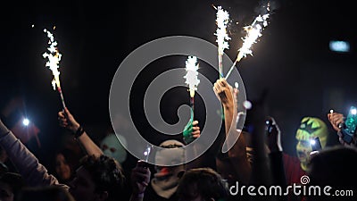 Fans Raise Hands with glowing sparklers in Front of Bright Colorful Strobing Lights on Stage. Stock Photo