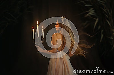 Fantasy medieval girl princess walks in dark gothic room. Woman queen is holding candlestick with burning candles in Stock Photo
