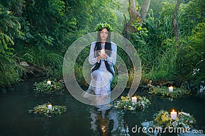 fantasy pagan witch slavic woman holding candle in hand. Divination summer tradition. Girl Mermaid nymph sits on banks Stock Photo