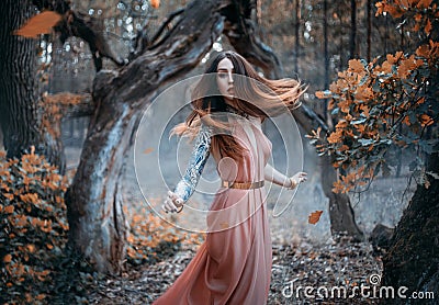 Fantasy portrait of a young red-haired woman in the autumn forest. The nymph girl runs and looks around. Long hair Stock Photo