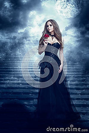 Fantasy Woman in Black Dress Smelling Rose Flower, Mystic Girl in Long Retro Gothic Gown Stock Photo