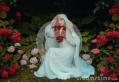 Fantasy woman in white vintage dress head covered with veil. Red-haired girl queen Medieval princess bride sits in Stock Photo