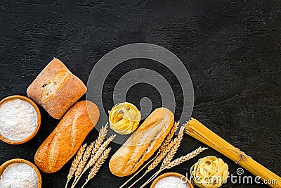 Farinaceous food. Fresh bread and raw pasta near flour in bowl and wheat ears on black background top view copy space Stock Photo