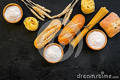 Farinaceous food. Fresh bread and raw pasta near flour in bowl and wheat ears on black background top view space for Stock Photo