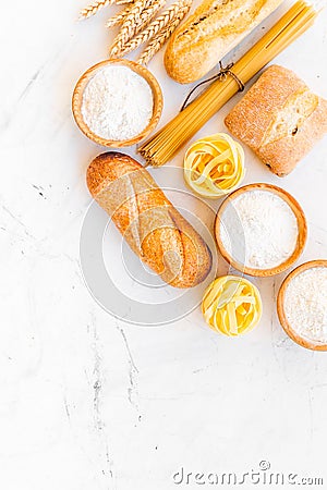 Farinaceous food. Fresh bread and raw pasta near flour in bowl and wheat ears on white stone background top view copy Stock Photo