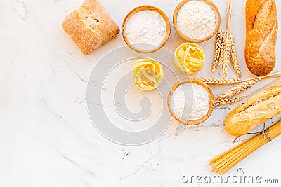 Farinaceous food. Fresh bread and raw pasta near flour in bowl and wheat ears on white stone background top view space Stock Photo