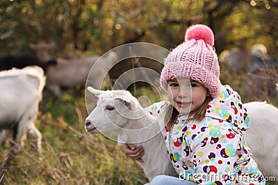 Farm animal. Cute little girl hugging goatling on pasture Stock Photo