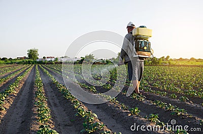 A farmer with a backpack spray sprays fungicide and pesticide on potato bushes. Protection of cultivated plants from insects Stock Photo