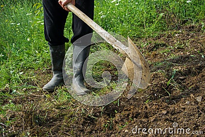 Farmer digging the soil with the shovel, young adult man with rubber boots Stock Photo