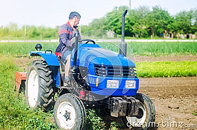 A farmer drives a tractor while working on a farm field. Loosening surface, cultivating the land. Farming, agriculture. Stock Photo
