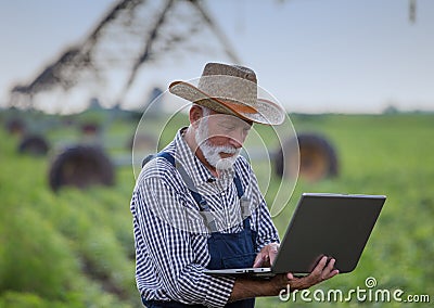 Farmer with laptop in front of irrigation system in field Stock Photo