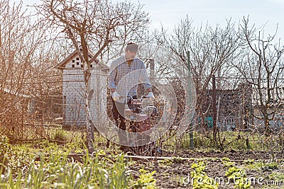 Farmer performing garden soil tillage with old poor cultivator tiller agricultural machine Stock Photo