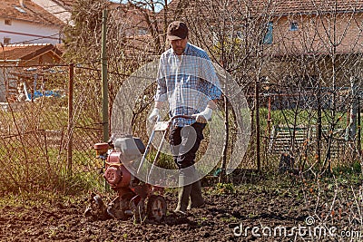 Farmer performing garden soil tillage with old poor cultivator tiller agricultural machine Stock Photo