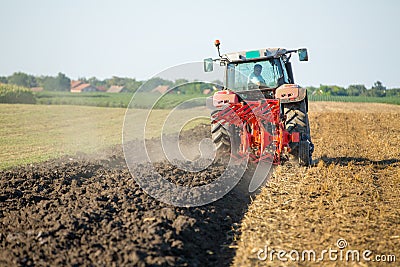 Farmer plowing stubble field with red tractor Stock Photo