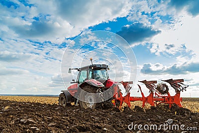 Farmer plowing stubble field with red tractor. Stock Photo