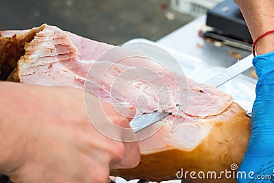 Butcher Slicing with Long Knife Smoked Baked Pork Ham from Leg at Market. Close up of Meat Texture Stock Photo