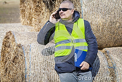 Farmer with smartphone and folder near the hay bales Stock Photo