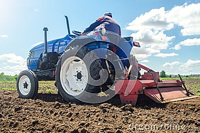Farmer on a tractor with a milling machine processes loosens soil in the farm field. Preparation for new crop planting. Grind Stock Photo