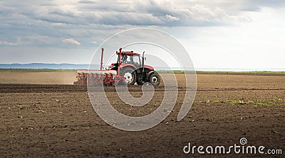 Farmer with tractor seeding crops at field Stock Photo