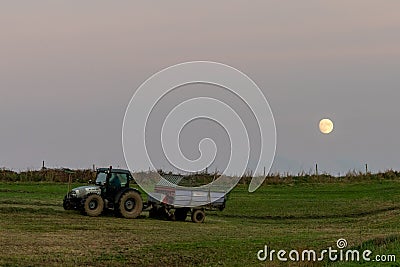 Farmer with tractor and trailer cultivating fields under a full moon at sunset Editorial Stock Photo