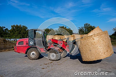 Farmer unloading round bales of straw with a front end loader Stock Photo