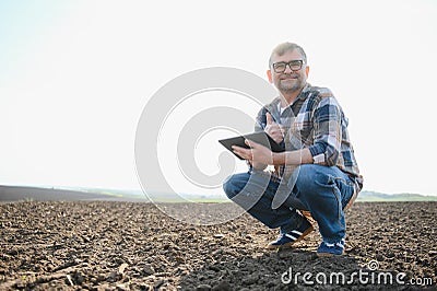 Farmer works in field in spring with tablet. An elderly farmer looks at tablet and green shoots. A smart, agronomist Stock Photo