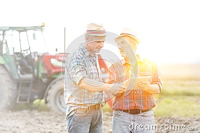 Farmers with digital tablet discussing at farm with yellow lens flare in background Stock Photo