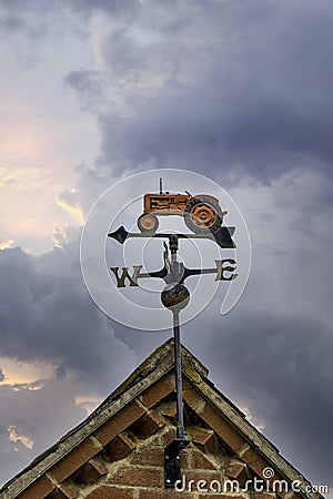 Farmers weathervane metal red old tractor on barn rooftop showing north east south west wind direction with arrow pointer in front Stock Photo