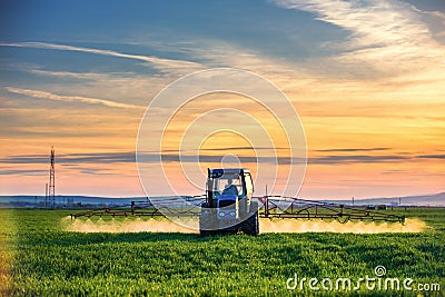 Farming tractor plowing and spraying on field, sunset Stock Photo