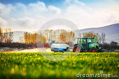 Farming tractor plowing and spraying on the green field Stock Photo