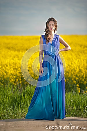 Fashion beautiful young woman in blue dress posing outdoor with cloudy dramatic sky in background. Attractive long hair brunette Stock Photo