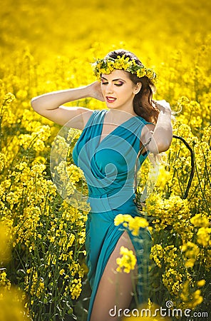 Fashion beautiful young woman in blue dress smiling in rapeseed field in bright sunny day Stock Photo