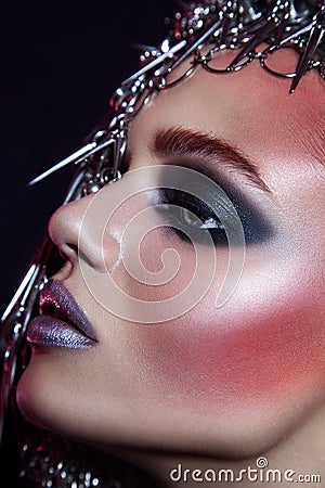 Fashion beauty model with metallic headwear and shiny silver red makeup and blue eyes and red eyebrows on black background Stock Photo