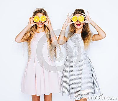 Fashion and beauty. Two stunning beauties girls having fun with slices of oranges closing by them eyes. Stock Photo