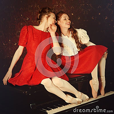 Fashion caucasian ballerinas sitting on the piano and laughing Stock Photo