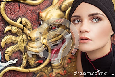 Fashion closeup of young woman with black hat over golden dragon on the wall Stock Photo